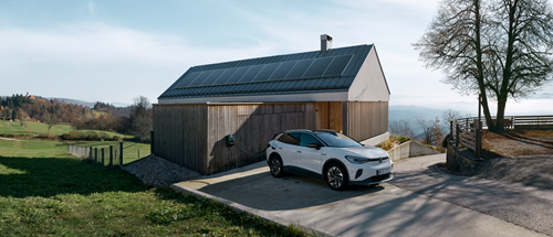 Auto steht vor Haus mit Solaranlage auf Dach vor Wasser und Natur