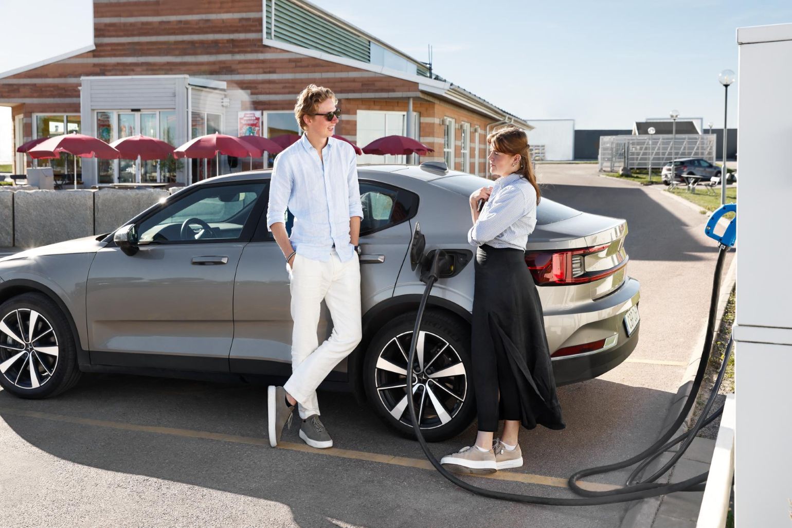 Paar lädt E-Auto auf einem Parkplatz vor einem Restaurant